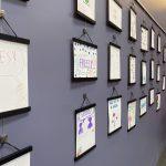 side view of a purple wall with white drawings framed in black hanging in a display.